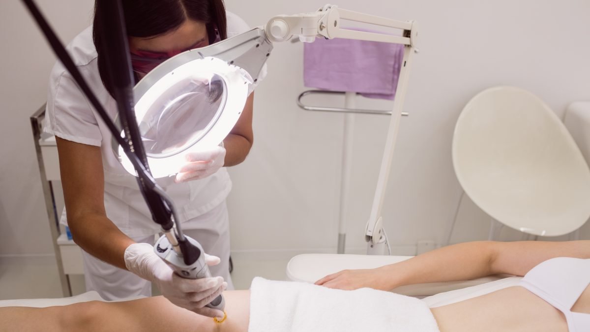 Técnica aplicando depilación láser en la pierna de una paciente en una cabina